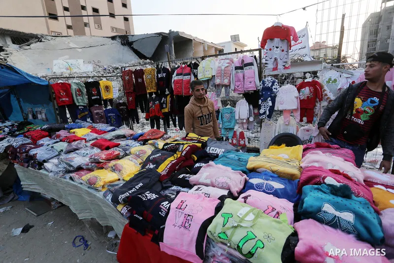Palestinian street vendors sell clothes near the rubble of al-Shuruq tower in Gaza City's al-Rimal neighbourhood which was targeted by Israeli strikes during the recent confrontations between Hamas and Israel, on Novembe...