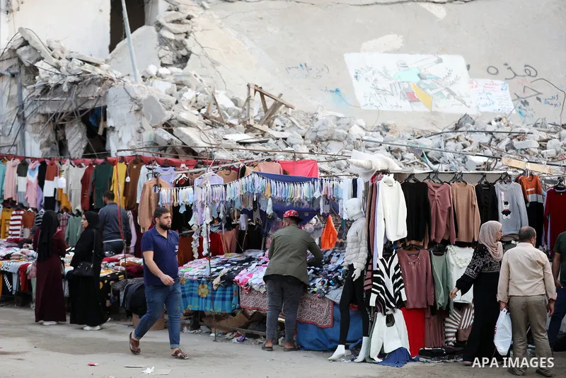Palestinian street vendors sell clothes near the rubble of al-Shuruq tower in Gaza City's al-Rimal neighbourhood which was targeted by Israeli strikes during the recent confrontations between Hamas and Israel, on Novembe...