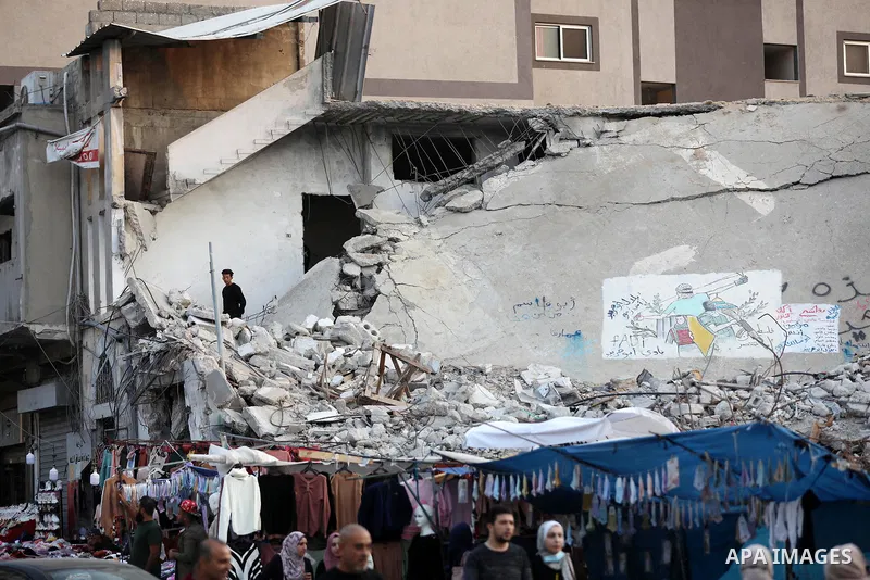 Palestinian street vendors sell clothes near the rubble of al-Shuruq tower in Gaza City's al-Rimal neighbourhood which was targeted by Israeli strikes during the recent confrontations between Hamas and Israel, on Novembe...