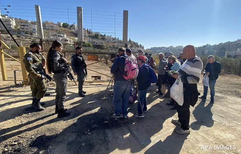 Palestinian farmers wait to enter to their lands that lie behind the separation wall to pick olives, in the West Bank city of Bethlehem on November 24, 2021. Photo by WAFA