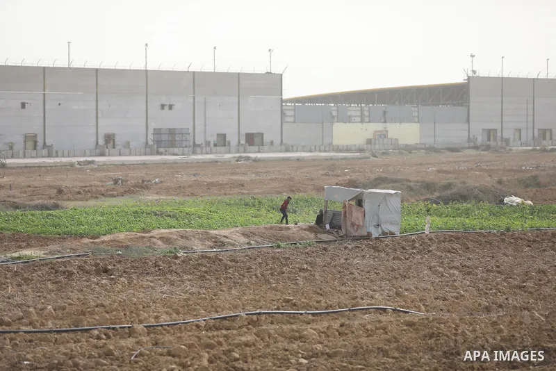 Palestinian farmers dig with hoes in a field near the portion of the high-tech barrier near the border between the Palestinian Gaza Strip and Israel, east of Gaza City on December 8, 2021. Photo by Ashraf Amra