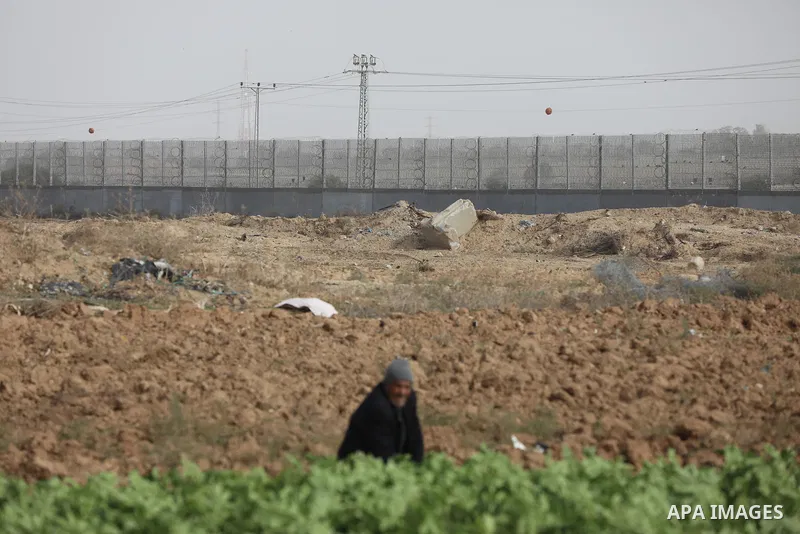 Palestinian farmers dig with hoes in a field near the portion of the high-tech barrier near the border between the Palestinian Gaza Strip and Israel, east of Gaza City on December 8, 2021. Photo by Ashraf Amra