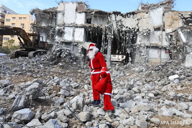 A Palestinian man and his son dressed as Santa Claus walk near the rubbles of al-Jawhara tower which was hit by Israeli strikes during the recent 11-day conflict between Israel and Hamas on May, on Christmas Eve, in Gaza...