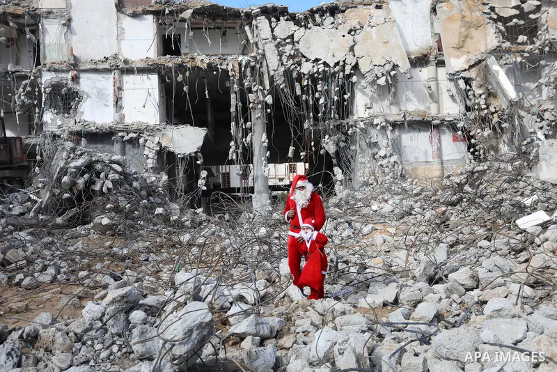 A Palestinian man and his son dressed as Santa Claus walk near the rubbles of al-Jawhara tower which was hit by Israeli strikes during the recent 11-day conflict between Israel and Hamas on May, on Christmas Eve, in Gaza...