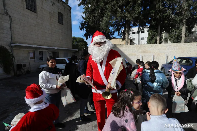 A Palestinian man, dressed as Santa Claus, distributes gifts to children outside the Church of Saint Porphyrios during Christmas celebrations in Gaza City, on December 24, 2021. Photo by Ashraf Amra