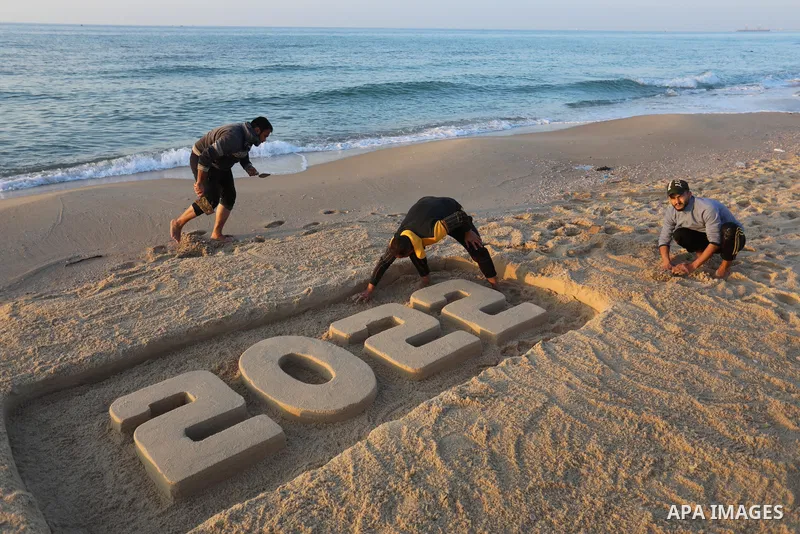 Palestinian youths paint on the sand sculpture "2022" at the beach of Beit Lahia in the nothern Gaza Strip, ahead of New Year, on December 28, 2021. Photo by Ashraf Amra