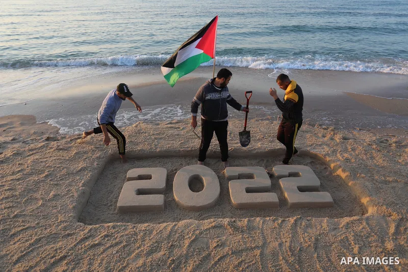 Palestinian youths paint on the sand sculpture "2022" at the beach of Beit Lahia in the nothern Gaza Strip, ahead of New Year, on December 28, 2021. Photo by Ashraf Amra