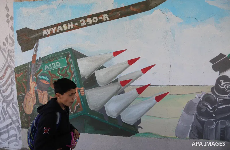 Palestinian students walk past a mural marking the 34th anniversary of the founding of the Hamas movement, in Khan Younis in the southern of Gaza strip on December 11, 2021. Photo by Ashraf Amra