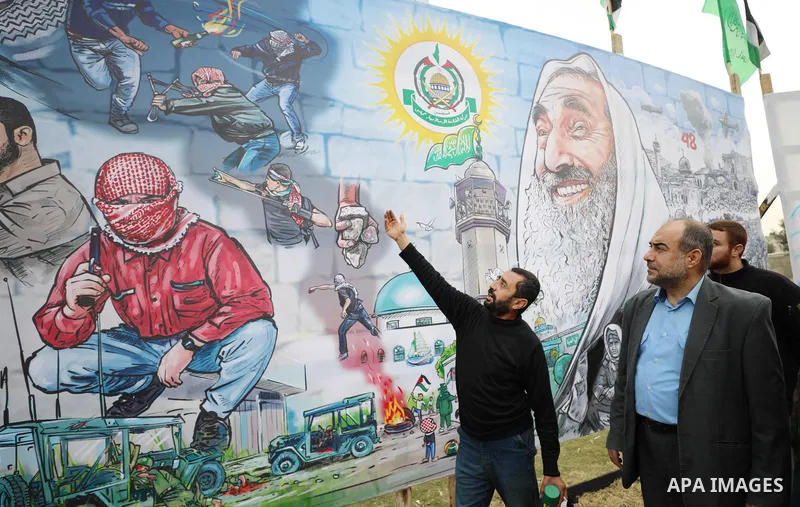 Palestinians gather around a mural marking the 34th anniversary of the founding of the Hamas movement, in Gaza city on December 12, 2021. Photo by Mahmoud Nasser