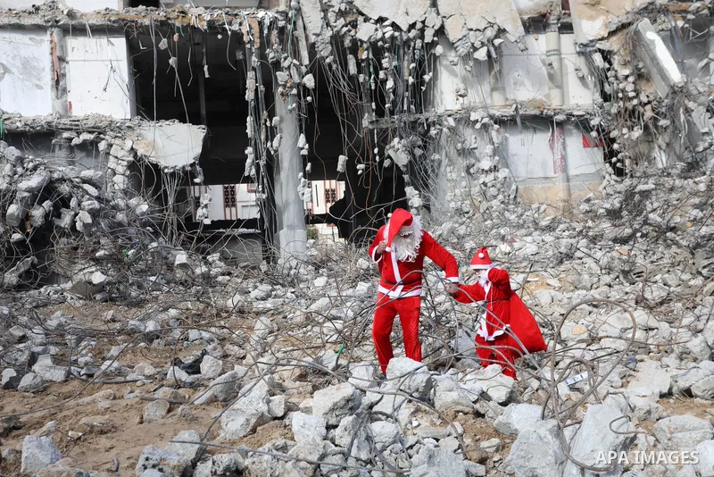 A Palestinian man and his son dressed as Santa Claus walk near the rubbles of al-Jawhara tower which was hit by Israeli strikes during the recent 11-day conflict between Israel and Hamas on May, on Christmas Eve, in Gaza...