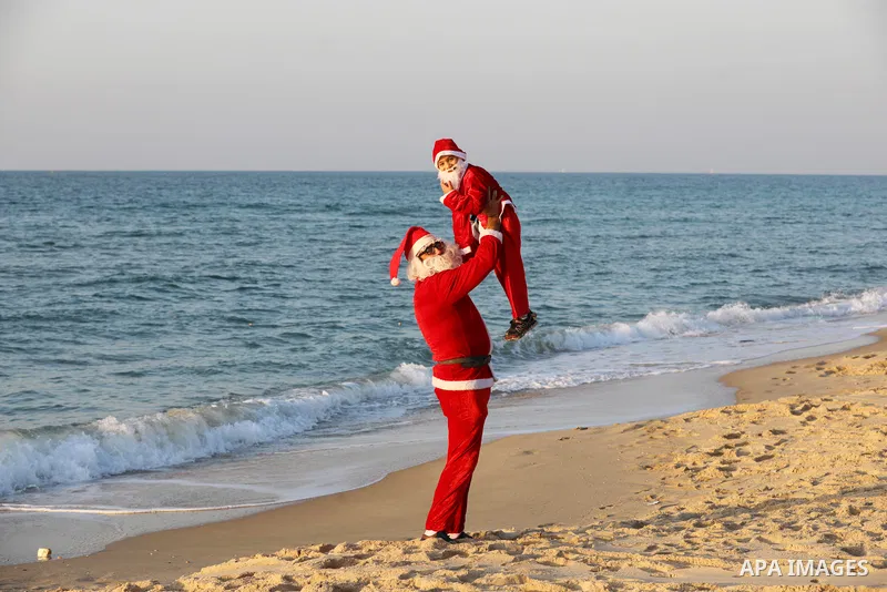 A Palestinian Christian man and his son dressed as Santa Claus walk along beach of in Beit Lahia sea in the northern of Gaza strip, on December 27, 2021. Photo by Ashraf Amra