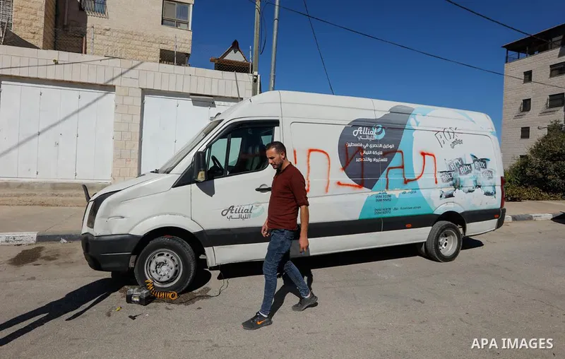 A Palestinian man inspects his vandalized vehicle and wall painted with Hebrew that reads "there will be a war over Judea and Samaria," after suspected Israeli settlers vandalized residents properties overnight in the We...