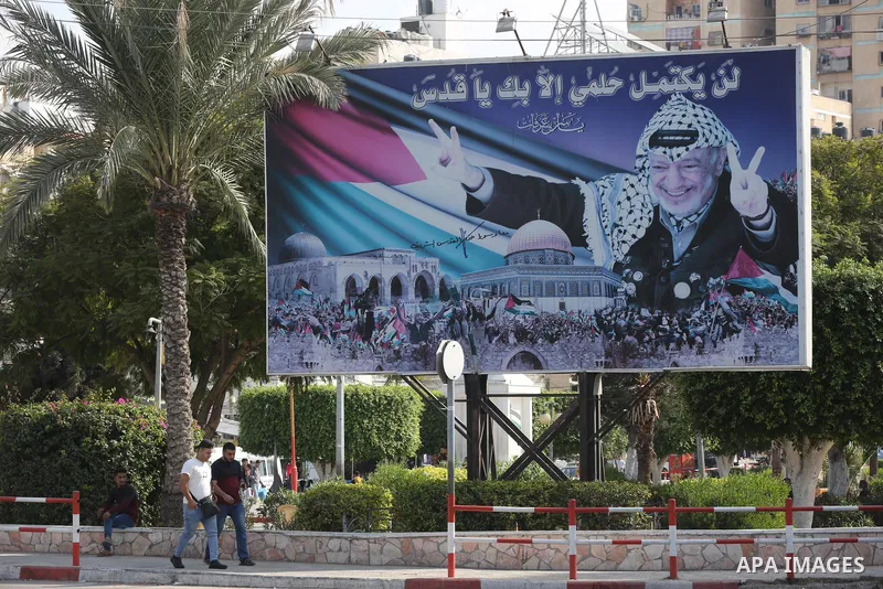 Palestinians walk past a photo depicting late president Yasser Arafat to mark the 17th anniversary of his death, in Gaza city on November 11, 2021. Photo by Ashraf Amra