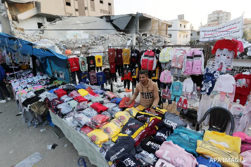 Palestinian street vendors sell clothes near the rubble of al-Shuruq tower in Gaza City's al-Rimal neighbourhood which was targeted by Israeli strikes during the recent confrontations between Hamas and Israel, on Novembe...