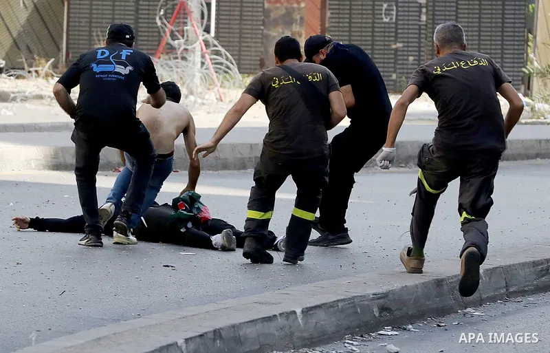 Men run to rescue a person shot while preparing to fire a rocket-propelled grenade, amidst clashes in the area of Tayouneh, in the southern suburb of the capital Beirut, on October 14, 2021. - Gunfire killed several peop...