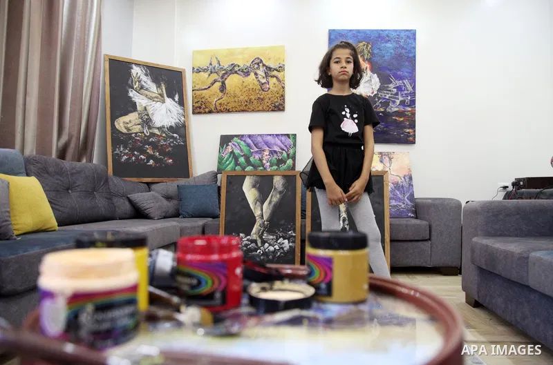 Palestinian artist Abeer Jibril's daughter dances ballet while Abeer Jibril is painting at home, in Gaza city on October 16, 2021. Jebril’s dark-coloured paintings show ballerinas chained in barbed wire, dancing on rocks...
