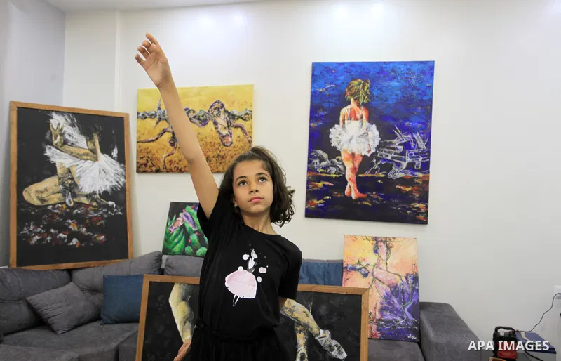 Palestinian artist Abeer Jibril's daughter dances ballet while Abeer Jibril is painting at home, in Gaza city on October 16, 2021. Jebril’s dark-coloured paintings show ballerinas chained in barbed wire, dancing on rocks...
