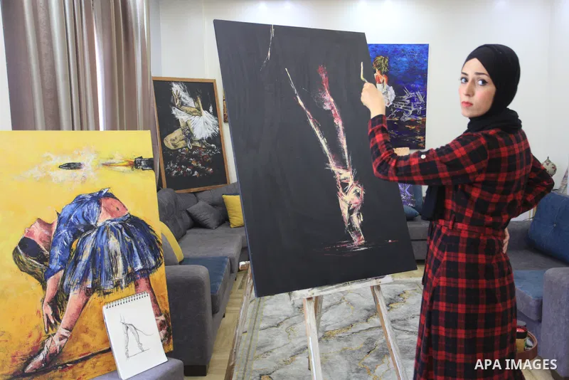 Palestinian artist Abeer Jibril's daughter dances ballet while Abeer Jibril is painting at home, in Gaza city on October 16, 2021. Jebril’s dark-coloured paintings show ballerinas chained in barbed wire, dancing on rocks...