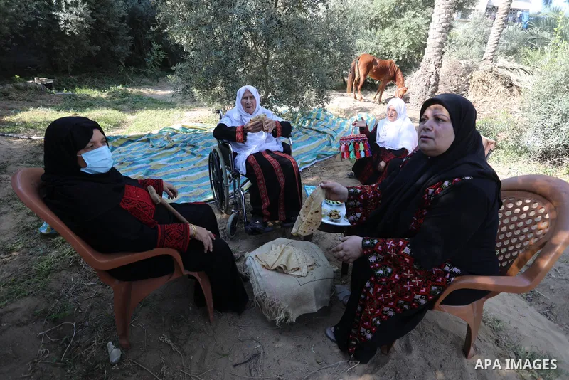 Palestinian women wear traditional dresses, as they pick olives during the harvest season, in Nuseirat camp in the central Gaza Strip, on 24 October 2021. Olive trees perform a crucial historical and cultural role in the...