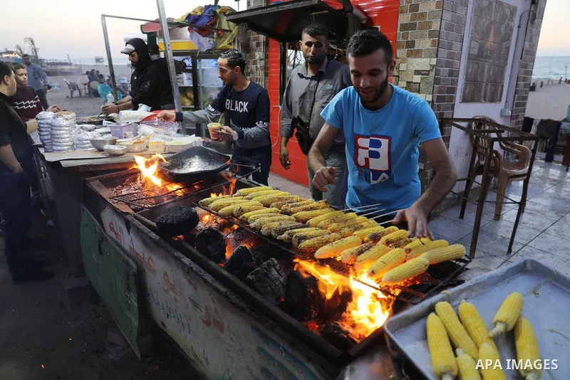 Palestinian men grill corn on the cob at a stall on Gaza City's seaside and sell it to customers, on October 26, 2021. Photo by Magdy Fathi