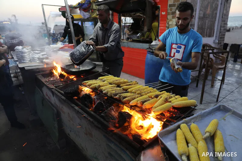 Palestinian men grill corn on the cob at a stall on Gaza City's seaside and sell it to customers, on October 26, 2021. Photo by Magdy Fathi