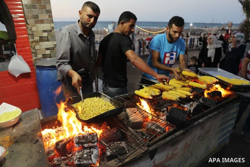 Palestinian men grill corn on the cob at a stall on Gaza City's seaside and sell it to customers, on October 26, 2021. Photo by Magdy Fathi