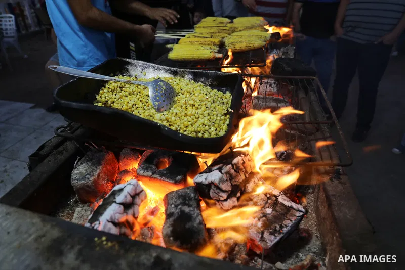 Palestinian men grill corn on the cob at a stall on Gaza City's seaside and sell it to customers, on October 26, 2021. Photo by Magdy Fathi