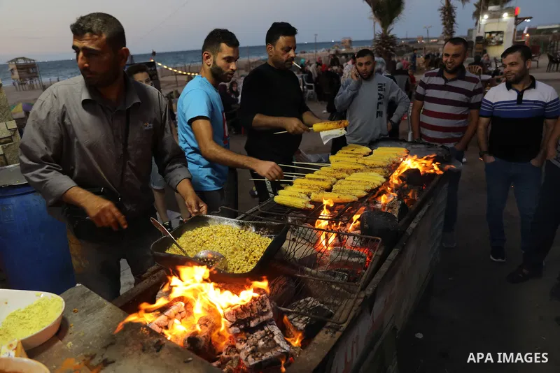 Palestinian men grill corn on the cob at a stall on Gaza City's seaside and sell it to customers, on October 26, 2021. Photo by Magdy Fathi