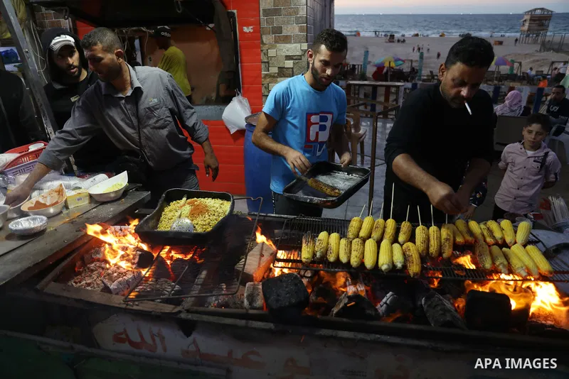Palestinian men grill corn on the cob at a stall on Gaza City's seaside and sell it to customers, on October 26, 2021. Photo by Magdy Fathi