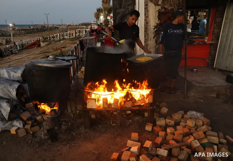 Palestinian men grill corn on the cob at a stall on Gaza City's seaside and sell it to customers, on October 26, 2021. Photo by Magdy Fathi
