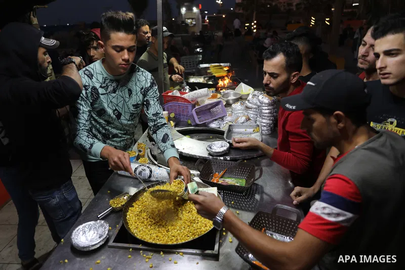 Palestinian men grill corn on the cob at a stall on Gaza City's seaside and sell it to customers, on October 26, 2021. Photo by Magdy Fathi