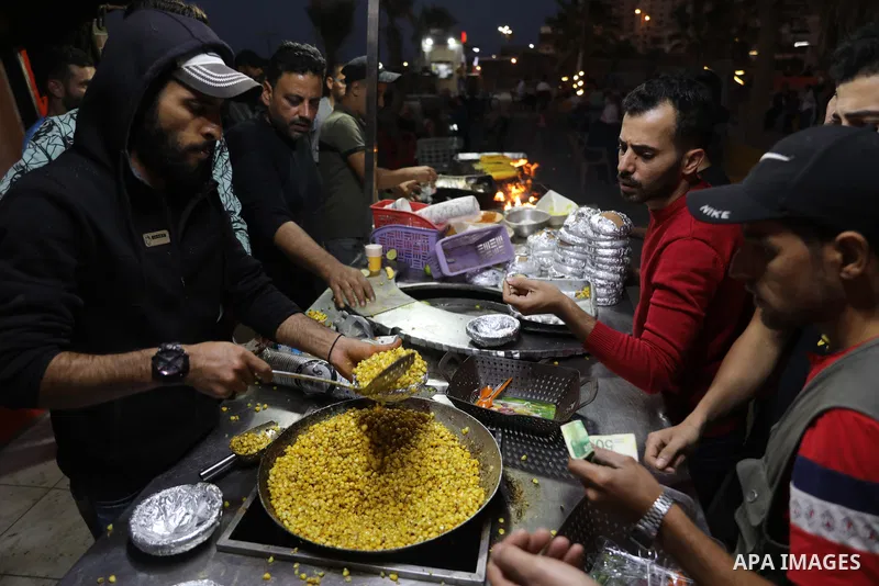 Palestinian men grill corn on the cob at a stall on Gaza City's seaside and sell it to customers, on October 26, 2021. Photo by Magdy Fathi