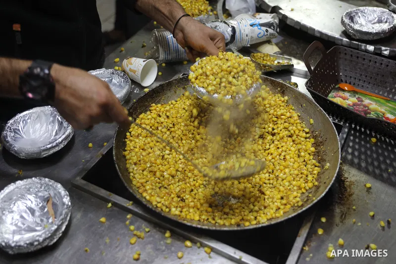 Palestinian men grill corn on the cob at a stall on Gaza City's seaside and sell it to customers, on October 26, 2021. Photo by Magdy Fathi