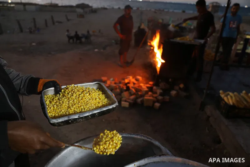 Palestinian men grill corn on the cob at a stall on Gaza City's seaside and sell it to customers, on October 26, 2021. Photo by Magdy Fathi