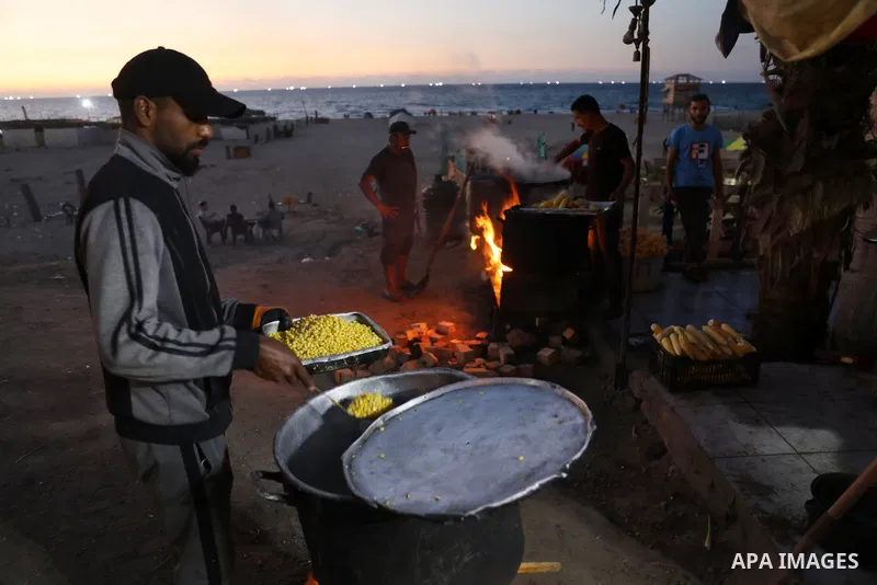 Palestinian men grill corn on the cob at a stall on Gaza City's seaside and sell it to customers, on October 26, 2021. Photo by Magdy Fathi