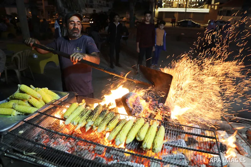 Palestinian men grill corn on the cob at a stall on Gaza City's seaside and sell it to customers, on October 26, 2021. Photo by Magdy Fathi