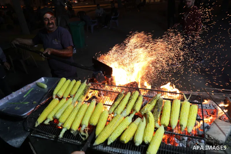 Palestinian men grill corn on the cob at a stall on Gaza City's seaside and sell it to customers, on October 26, 2021. Photo by Magdy Fathi