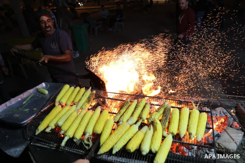 Palestinian men grill corn on the cob at a stall on Gaza City's seaside and sell it to customers, on October 26, 2021. Photo by Magdy Fathi