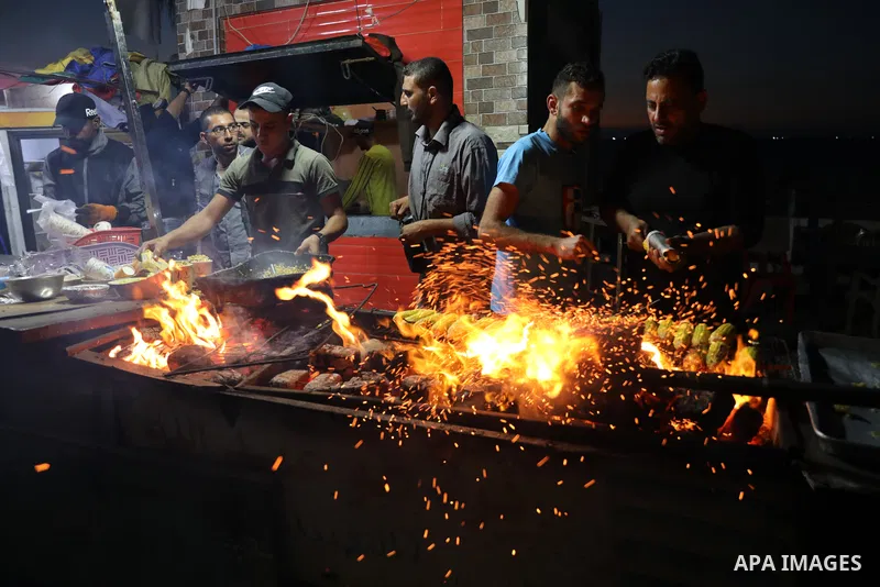 Palestinian men grill corn on the cob at a stall on Gaza City's seaside and sell it to customers, on October 26, 2021. Photo by Magdy Fathi