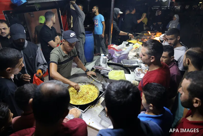 Palestinian men grill corn on the cob at a stall on Gaza City's seaside and sell it to customers, on October 26, 2021. Photo by Magdy Fathi