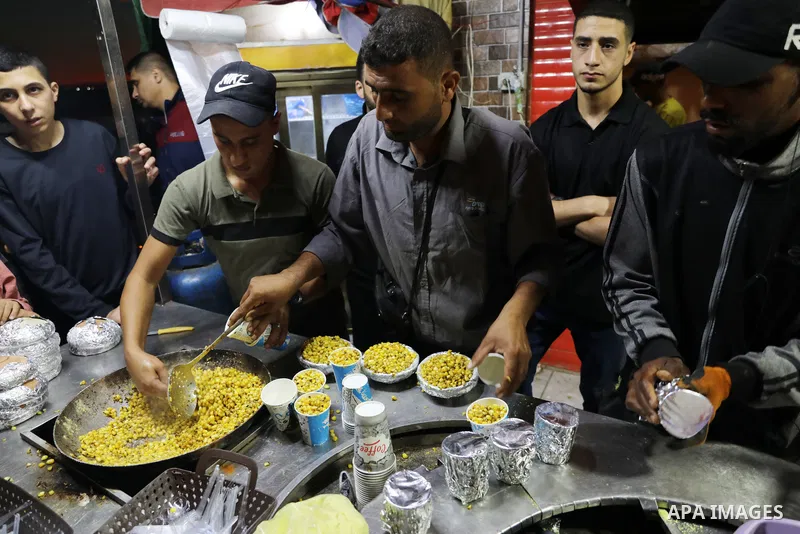 Palestinian men grill corn on the cob at a stall on Gaza City's seaside and sell it to customers, on October 26, 2021. Photo by Magdy Fathi