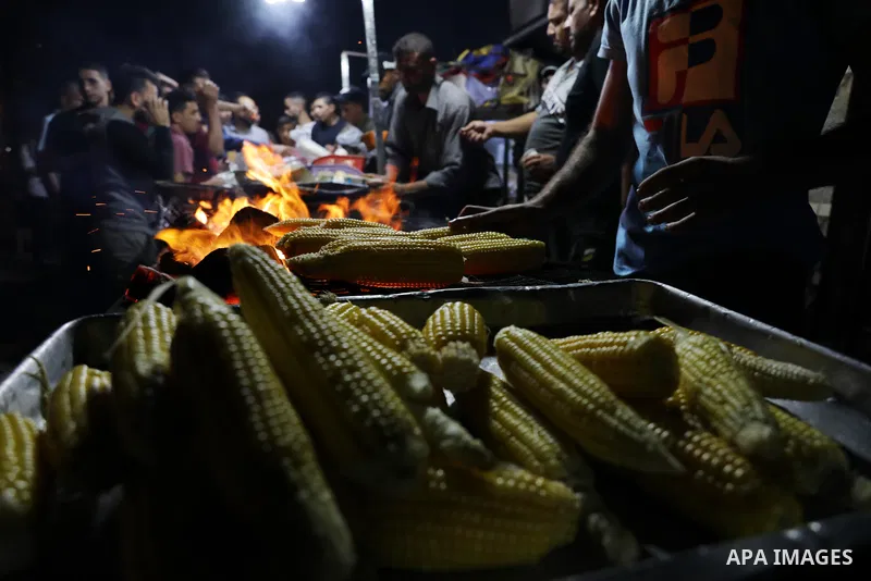 Palestinian men grill corn on the cob at a stall on Gaza City's seaside and sell it to customers, on October 26, 2021. Photo by Magdy Fathi