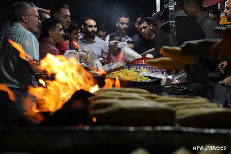 Palestinian men grill corn on the cob at a stall on Gaza City's seaside and sell it to customers, on October 26, 2021. Photo by Magdy Fathi