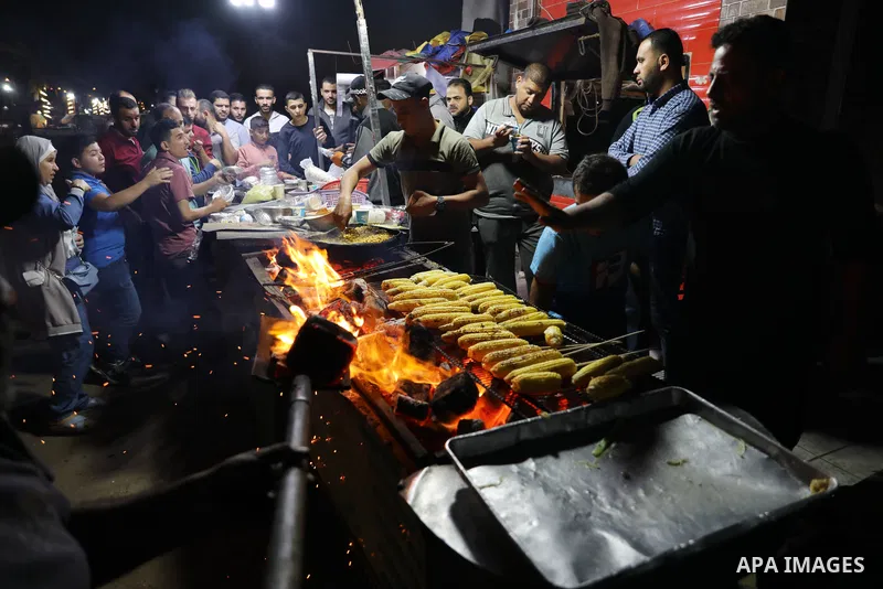Palestinian men grill corn on the cob at a stall on Gaza City's seaside and sell it to customers, on October 26, 2021. Photo by Magdy Fathi