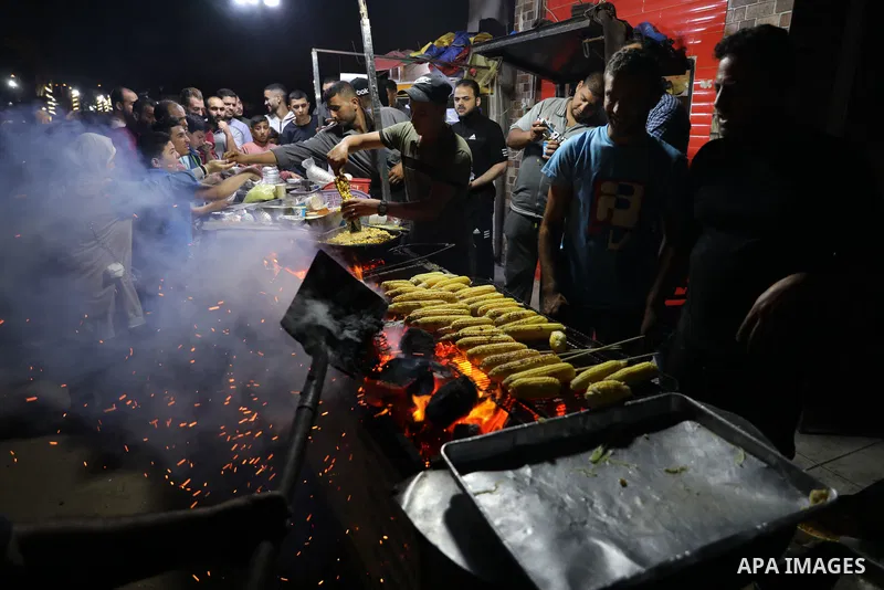 Palestinian men grill corn on the cob at a stall on Gaza City's seaside and sell it to customers, on October 26, 2021. Photo by Magdy Fathi