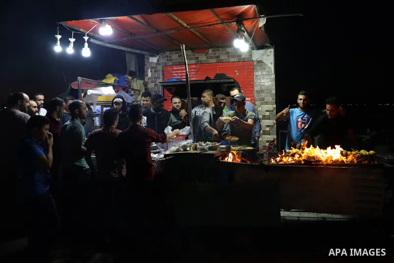 Palestinian men grill corn on the cob at a stall on Gaza City's seaside and sell it to customers, on October 26, 2021. Photo by Magdy Fathi