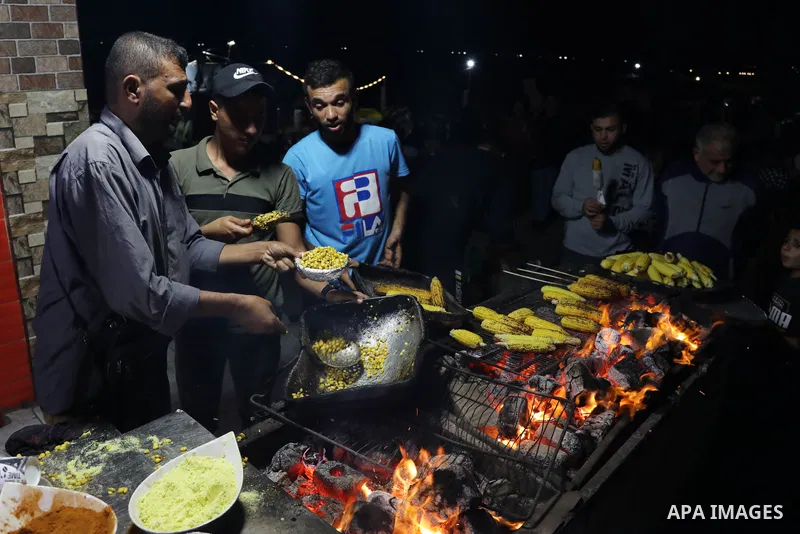 Palestinian men grill corn on the cob at a stall on Gaza City's seaside and sell it to customers, on October 26, 2021. Photo by Magdy Fathi