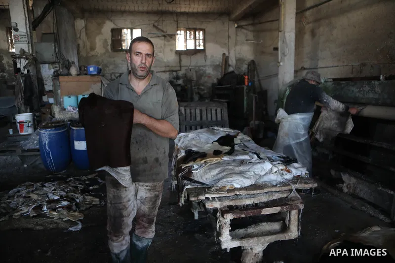 Palestinian workers paint leather and putting pieces out to dry as part of the finish process of leather tanning in a small factory to sell it to manufacture of shoes, in the West Bank city of Hebron on October 27, 2021....