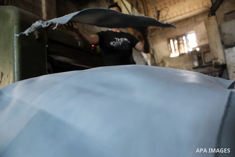 Palestinian workers paint leather and putting pieces out to dry as part of the finish process of leather tanning in a small factory to sell it to manufacture of shoes, in the West Bank city of Hebron on October 27, 2021....