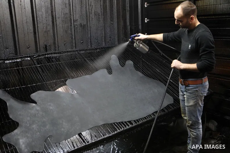Palestinian workers paint leather and putting pieces out to dry as part of the finish process of leather tanning in a small factory to sell it to manufacture of shoes, in the West Bank city of Hebron on October 27, 2021....